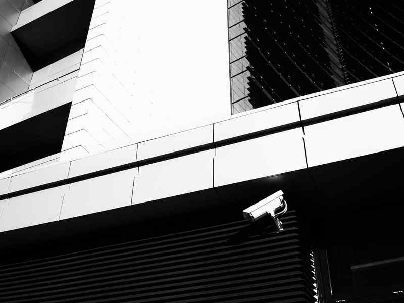 A security camera under the edge of a modern office building.