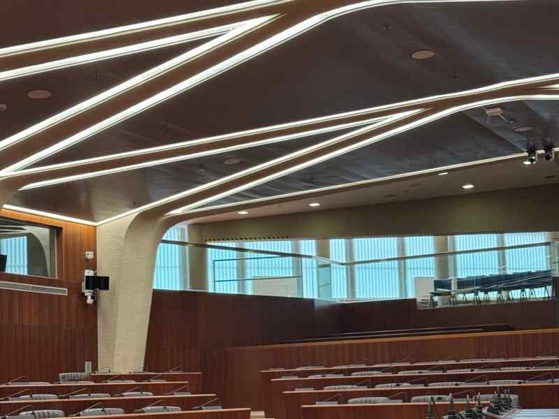 An empty council chamber with wooden desks and a microphone at every seat.